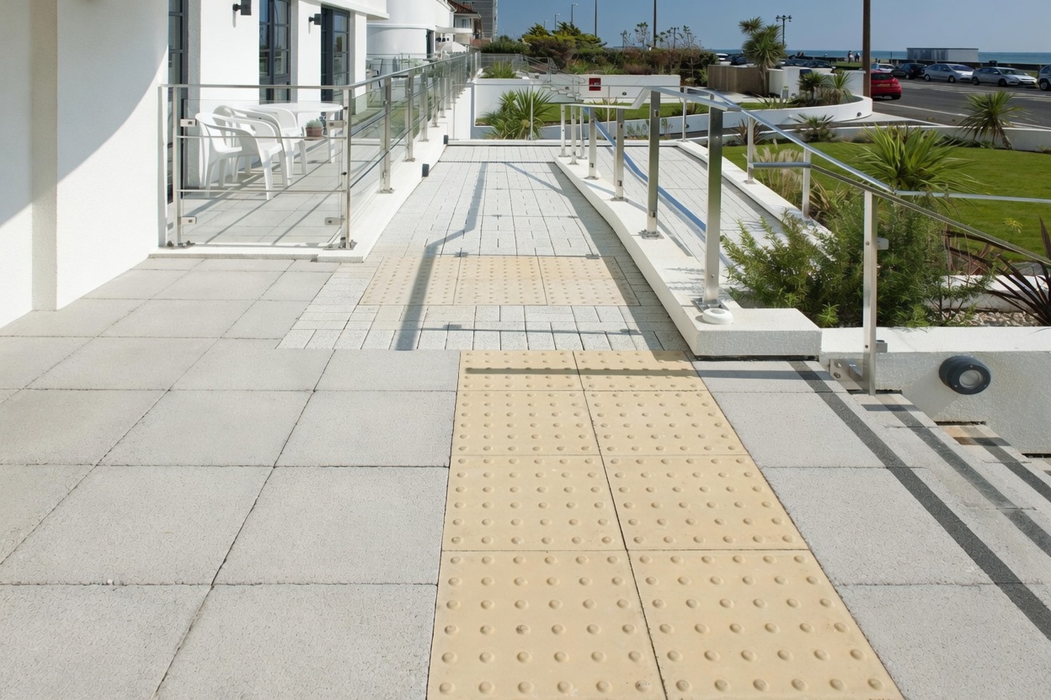 Tactile DDA paving on a stone-clad commercial accessibility ramp with stainless rails
