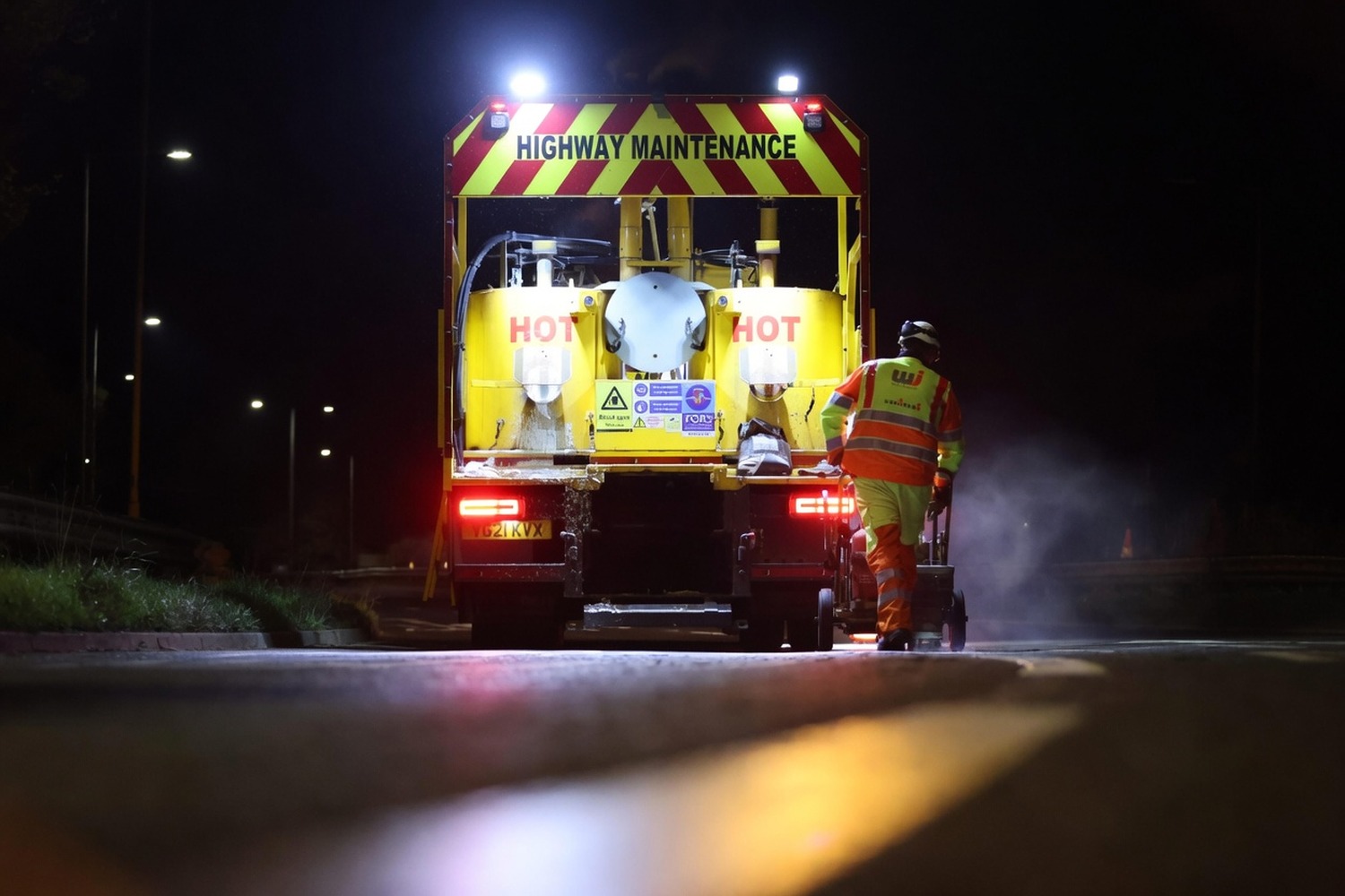 Operative behind a highway-maintenance truck applying hot thermoplastic markings on a live carriageway at night